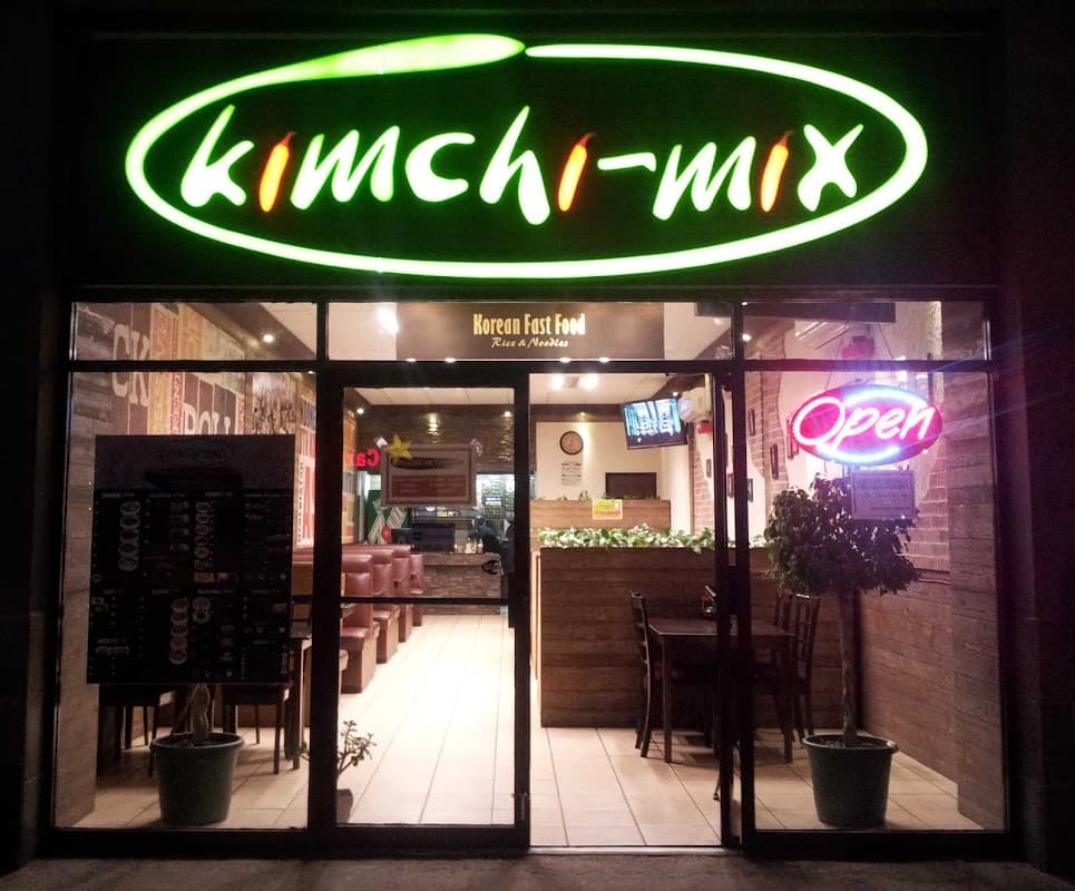 Fachada de Kimchimix con su letrero iluminado y la calle de Calz del Tecnológico al fondo