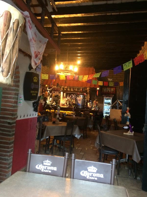 Exterior iluminado de La Antigua Chiripa con su letrero de neón y una mesa con una jarra de cerveza artesanal y un plato de fajitas al carbón