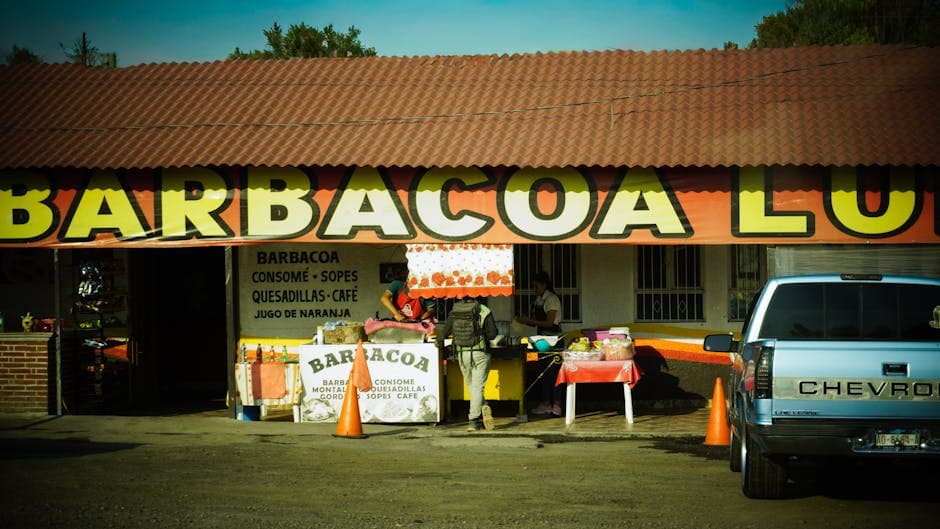 Outdoor view of a Mexican barbacoa restaurant with a truck and food stall.