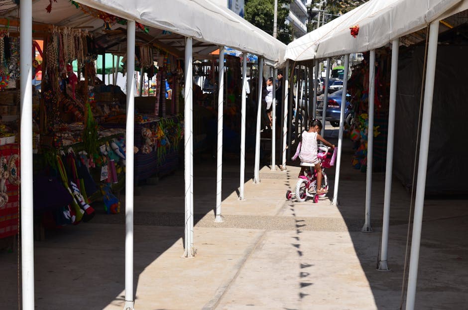 A young girl rides a bicycle through market stalls in Guerrero, Mexico, on a sunny day.