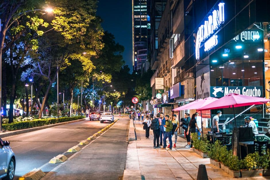 Lively street scene in Mexico City featuring people, restaurants, and illuminated storefronts at night.