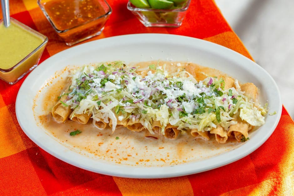 Appetizing Mexican taquitos topped with cheese and lettuce, served with assorted salsas and lime.