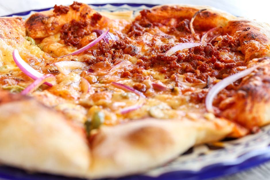 Close-up of a cheesy pizza topped with pepperoni, red onions, and spices, freshly baked.