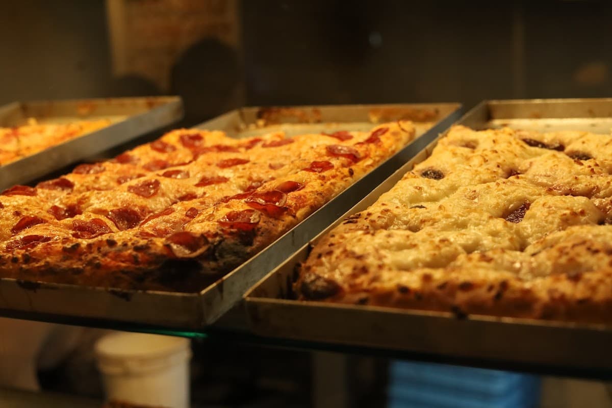 Vista del interior de Coma Pizza Polanco con mesas ocupadas, luces tenues y una pizza Detroit con trufa sobre la mesa