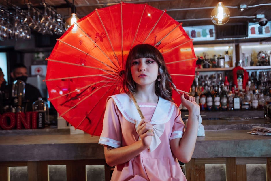 A stylish young woman holding a red parasol, seated indoors at a bar, creating a vibrant and fashionable scene.