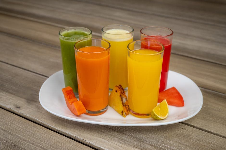 Colorful array of fresh fruit juices in glasses on a white plate with assorted fruits.
