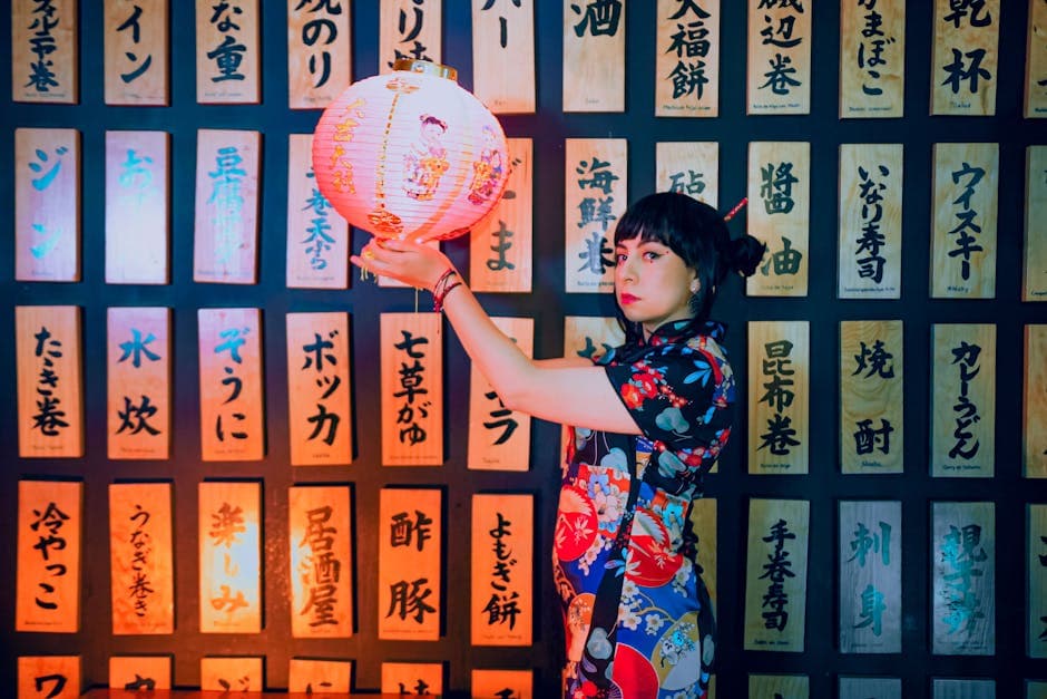 A woman in traditional attire holding a Japanese lantern against a backdrop of Japanese writings.
