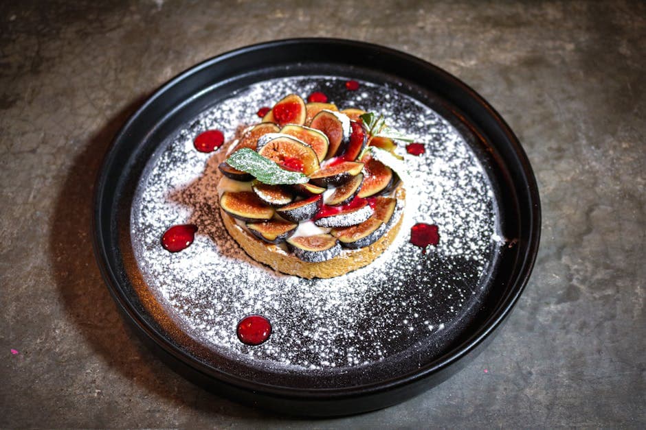 Delicious fig tart topped with powdered sugar and garnished with mint on a dark plate.