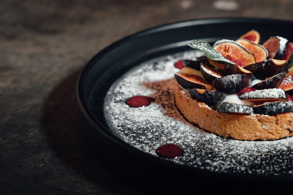 Gourmet fig tart beautifully arranged on a dark plate with artistic presentation.