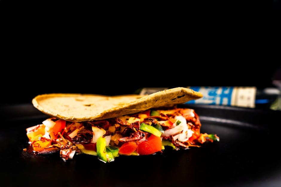 Close-up of a vibrant Mexican taco filled with fresh vegetables against a dark background.