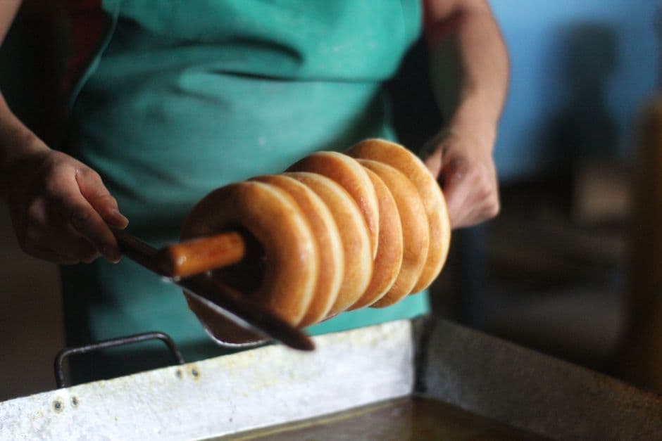 A person making traditional Mexican bread, frying multiple rolls on a stick indoors.