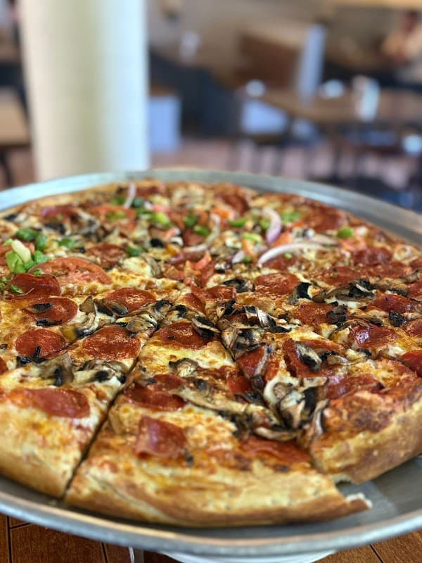 Vista exterior de Gabacho´s Pizzeria Ixtlahuacan con su letrero iluminado y una mesa con pizza de pepperoni