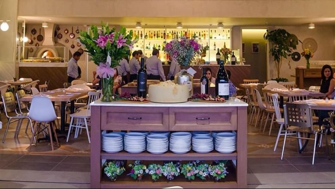 Fachada de Assaggio Italian Cuisine en Pueblo Serena, con su letrero iluminado y clientes entrando al atardecer