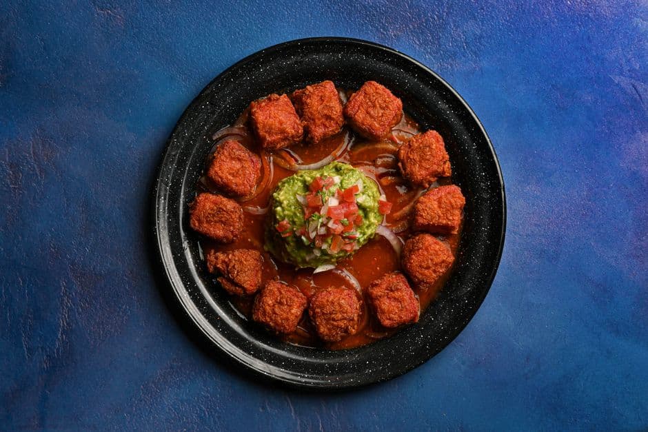 Delicious Mexican meatballs served with guacamole over a vibrant blue background.