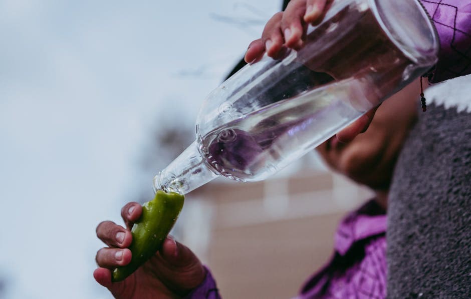 A person pouring water from a bottle into a green chili pepper outdoors in Oaxaca, Mexico.