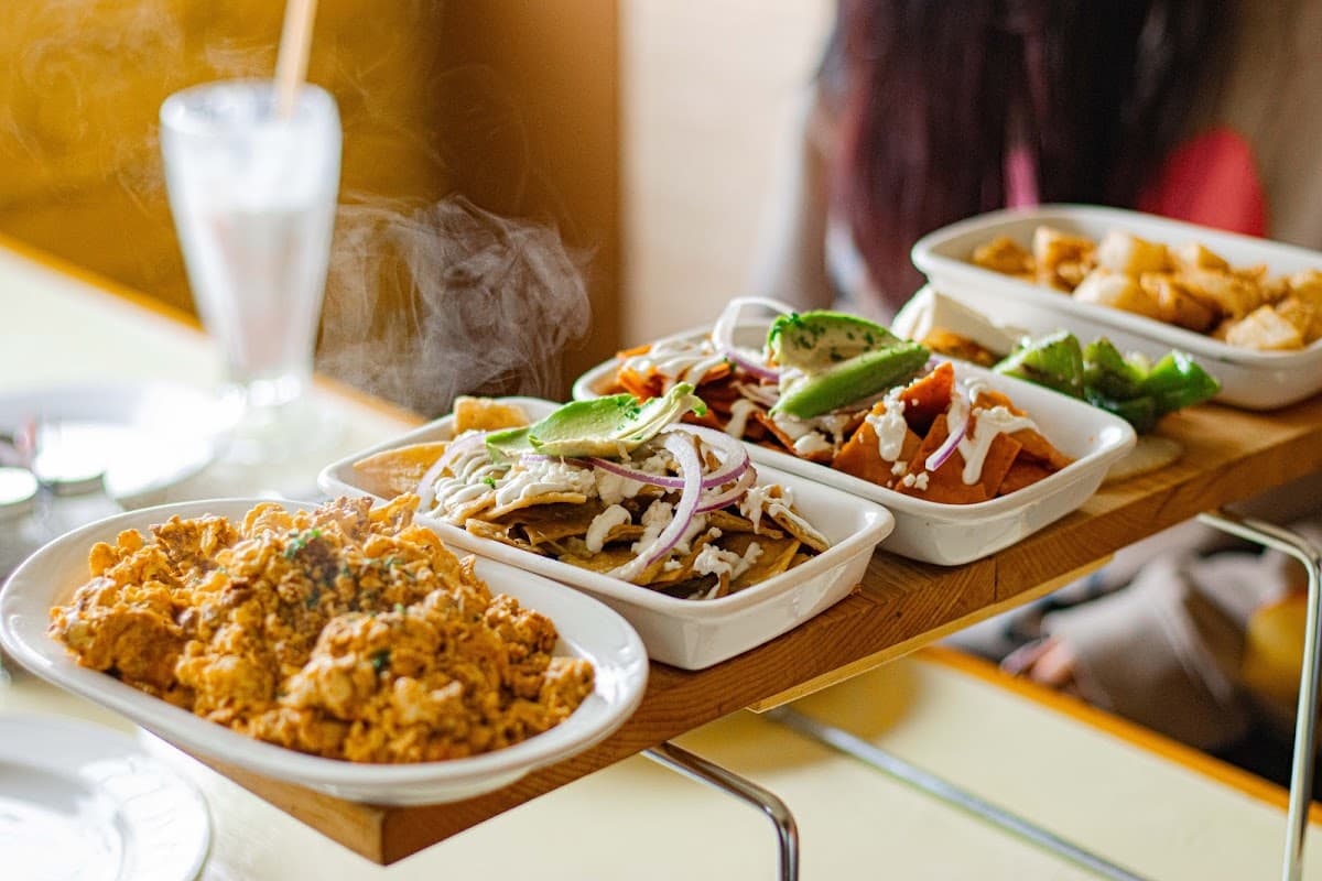 El Encino — fachada de madera bajo luces cálidas, mesa con tacos de carne asada y salsa verde.