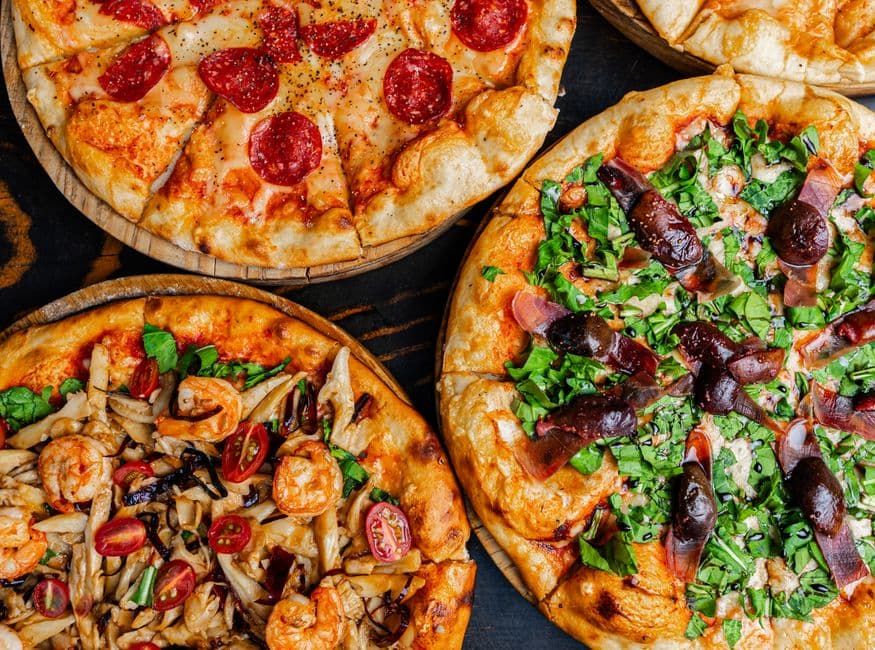 Top view of assorted gourmet pizzas with diverse and colorful toppings, perfect for Italian cuisine lovers.