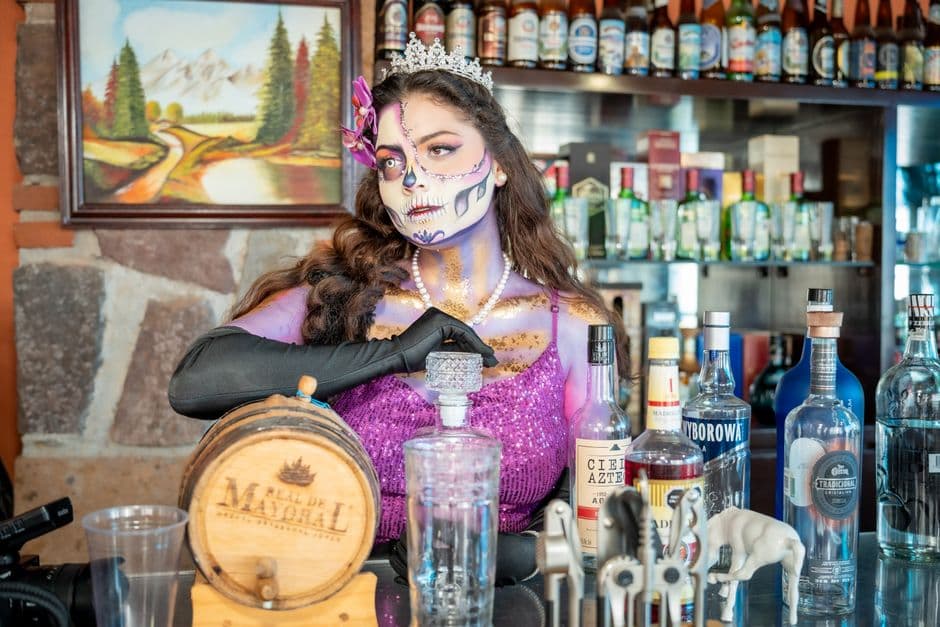 Elegant Catrina makeup with colorful attire in a vibrant Mexican bar setting, CDMX.