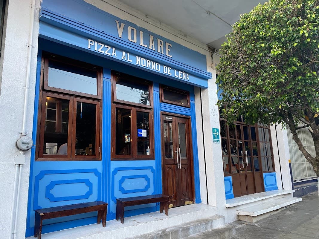 Volare Pizzería y Restaurante — fachada con letrero iluminado y mesas al aire libre