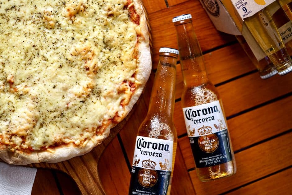 Top view of a cheese pizza and Corona beers on a wooden table. Perfect meal setup.