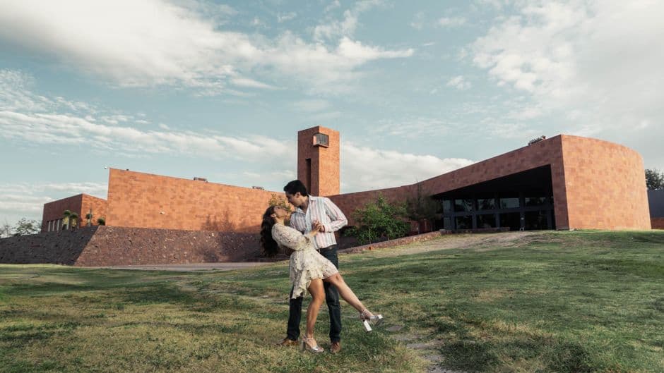 A couple shares a romantic dance outside a unique architectural building on a sunny day.