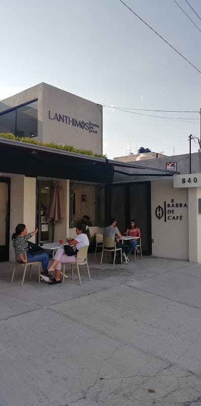 Fachada de Lanthimos Barra de Café en Valentín Gama, con su letrero retro iluminado y mesas exteriores bajo sombra de árboles
