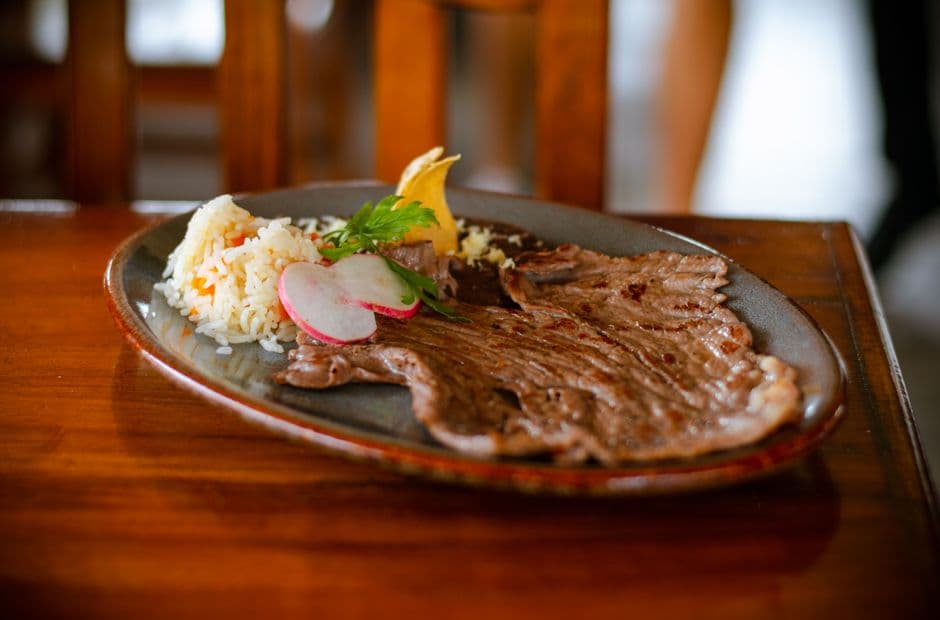 Delicious Mexican grilled beef with rice, radish, and lemon on a plate, served indoors.