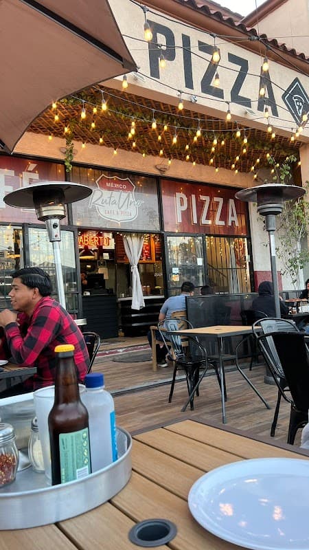 Exterior de Ruta Uno Café y Pizza en Lib. Sur 6237, con su letrero iluminado y clientes en la terraza al atardecer
