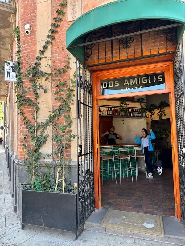 Exterior iluminado de Dos Amigos Café‑Bar con mesas al aire libre y letrero visible — foto de noche