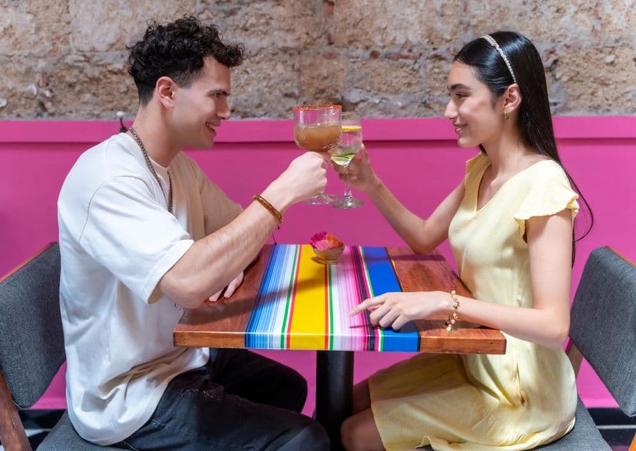 A couple enjoying a romantic toast with colorful cocktails at a vibrant cafe in CDMX, Mexico.
