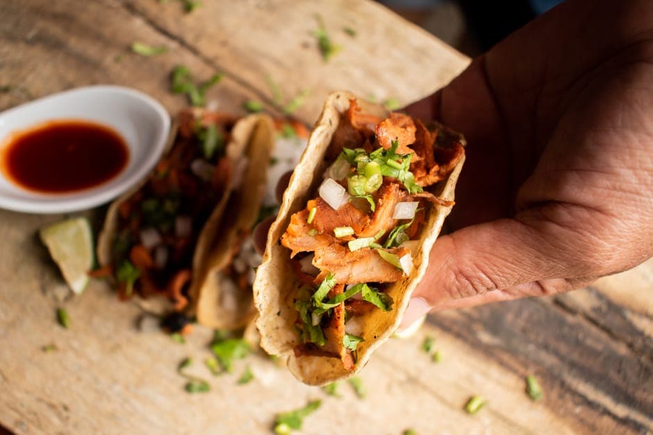 Close-up of a hand holding Mexican tacos filled with fresh ingredients on a wooden table.