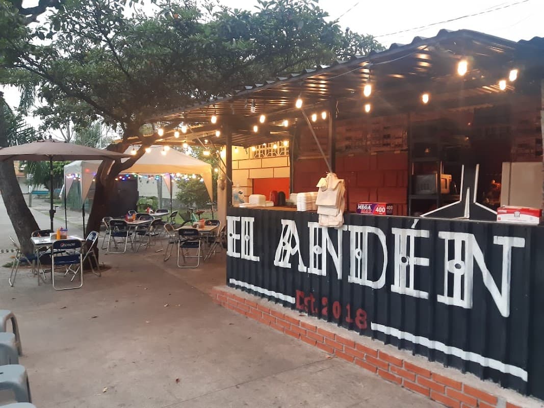 Exterior de EL ANDÉN Est. 2018 Yanga con su letrero iluminado y una fila de clientes esperando, captura la vibra del barrio