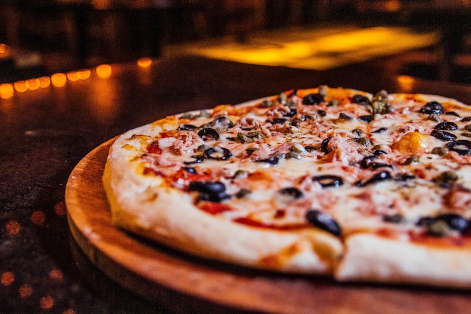 Close-up of a vegetable pizza with olives on a wooden board in a cozy restaurant setting.