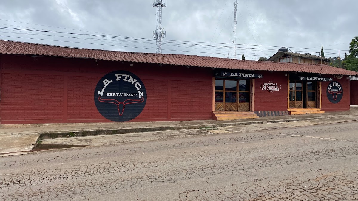 Exterior de Restaurant La Finca con su jardín y mesas al aire libre, mostrando una parrilla con hamburguesa y huarache al frente
