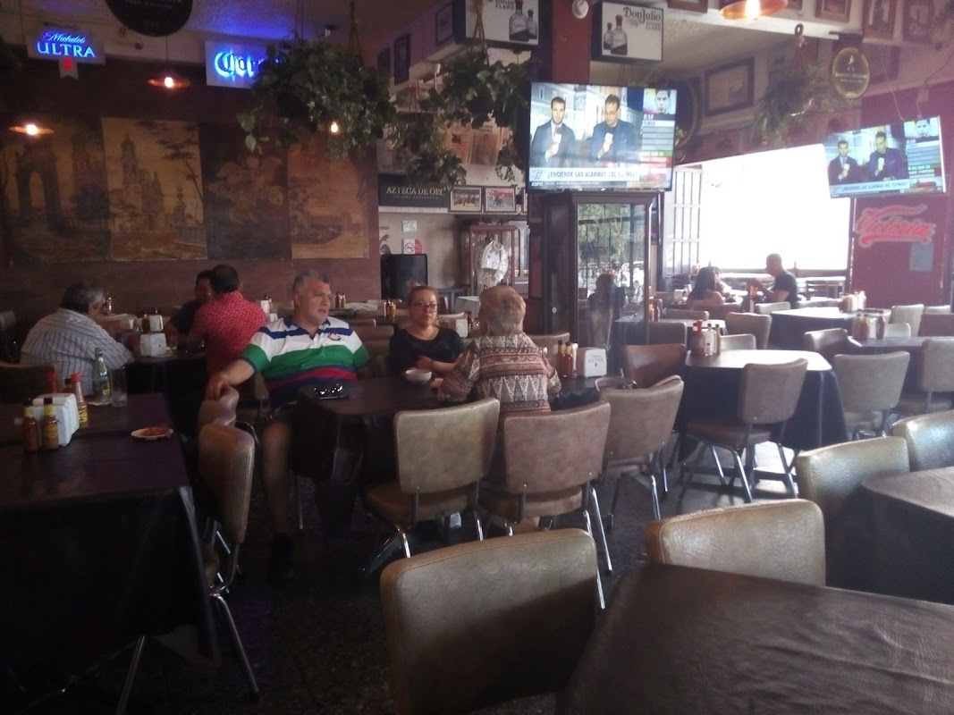 Terraza de Merendero San Marcos con músicos de mariachi y una tabla de botanas bajo luces de neón