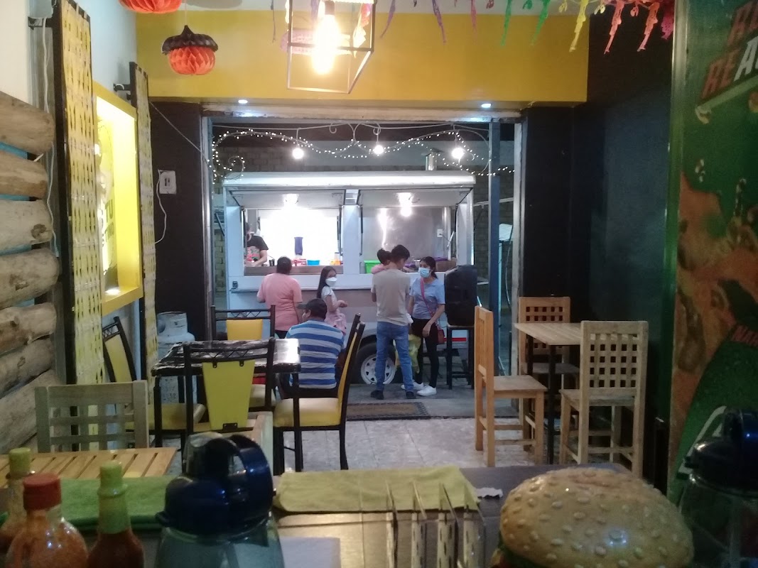 Buguis con su mostrador de hamburguesas, resaltando una hamburguesa doble con papas fritas y una cerveza en vaso