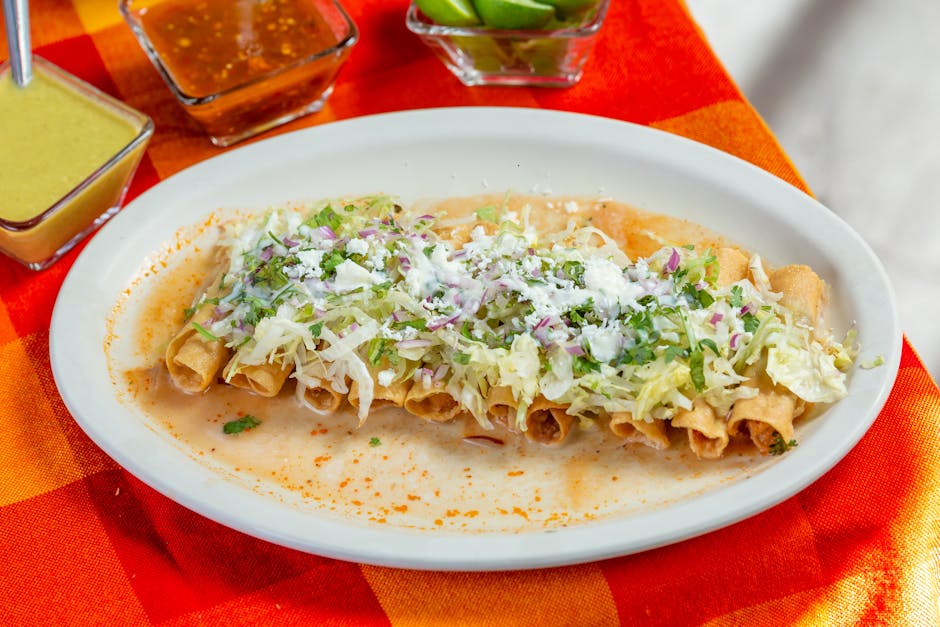 Appetizing Mexican taquitos topped with cheese and lettuce, served with assorted salsas and lime.