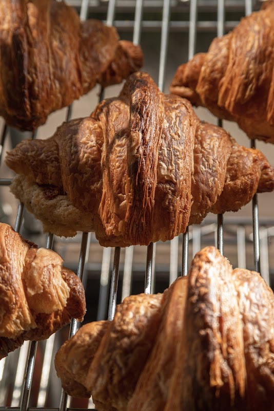 Interior de Amento Panadería mostrando la barra de exhibición con croissants, panes dulces y una taza de café humeante.