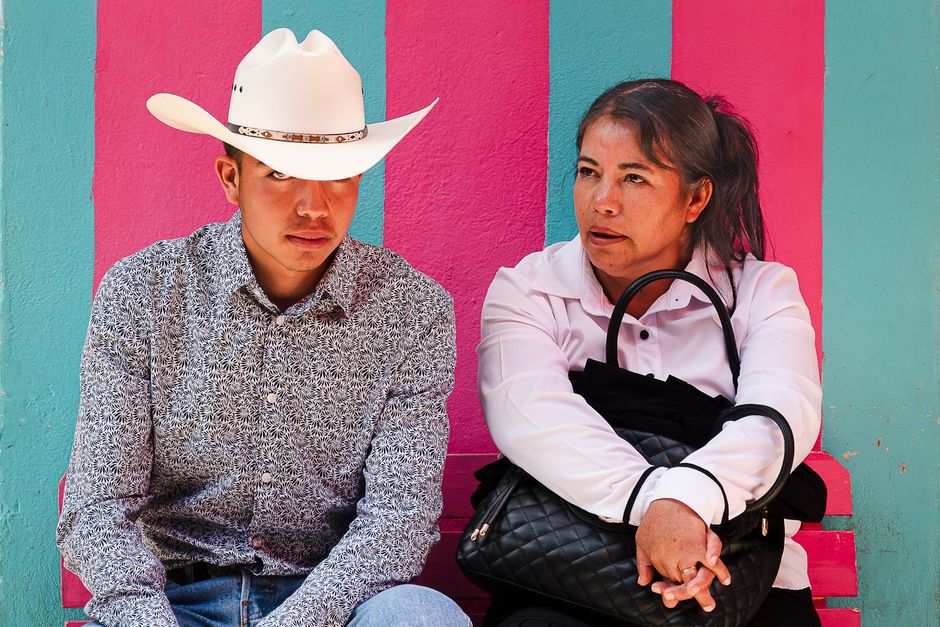 A man and woman in conversation against a vibrant wall in Atotonilco el Grande, Mexico.