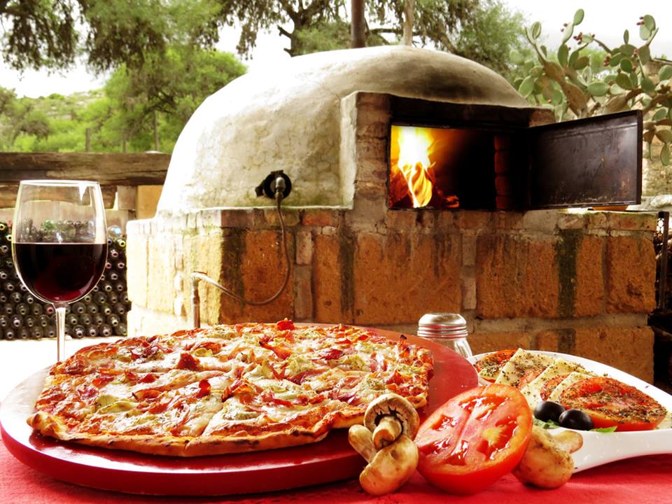 Armadilli Pizzeria — interior con horno de leña encendido y una pizza margarita recién salida, mesa de madera