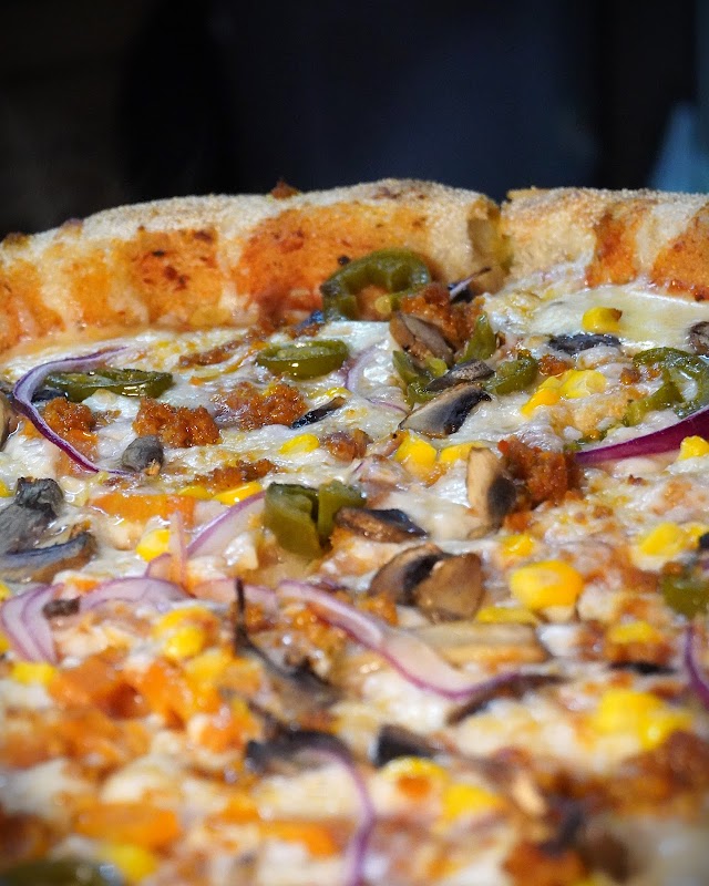 Fachada de Don Chipotle y Don Que chow con su letrero colorido y mesas al aire libre, mostrando una pizza recién salida del horno