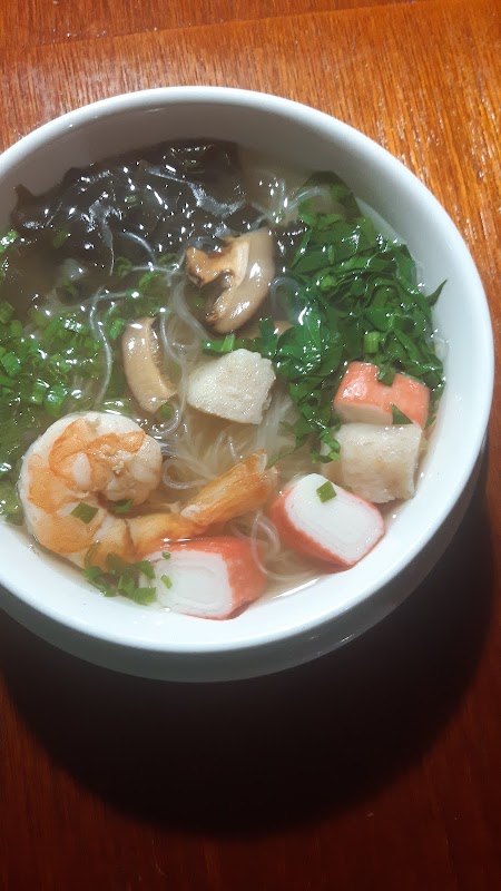 Interior de Ōchō cocina japonesa con barra de ramen humeante y platos de sushi sobre la mesa