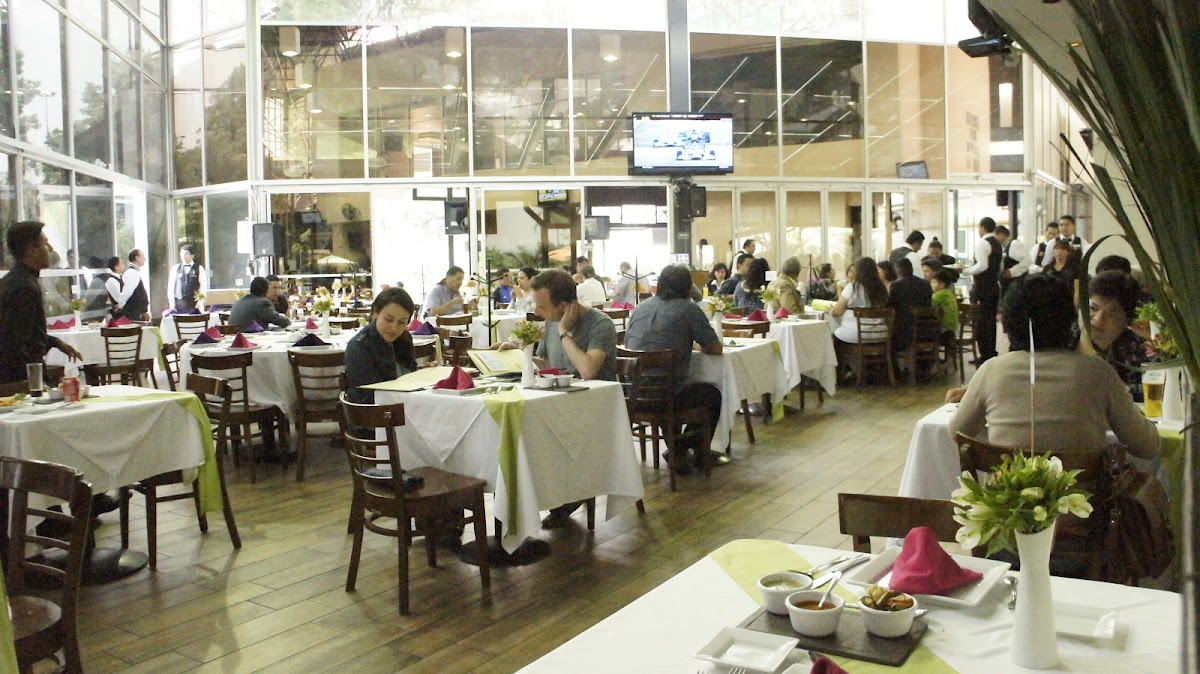 Interior del comedor con mesas de madera y luz natural que entra del jardín, clientes disfrutando