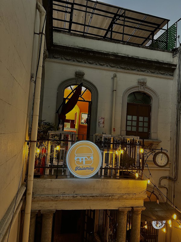Interior de Kalamity Burgers, mesa de madera, luces tenues y camarero sirviendo un batido de fresa con trozos de fruta