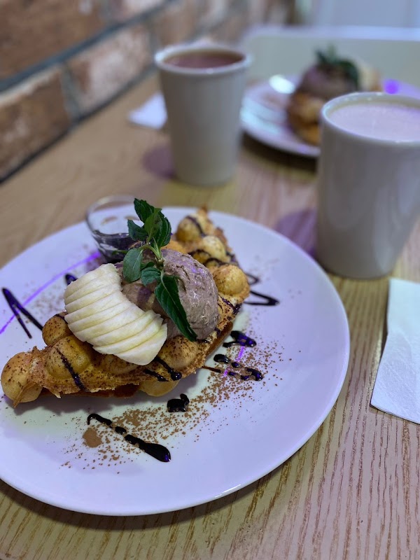 Waffle de avellana en un plato blanco, con azúcar glas y una bola de helado, resaltando la textura crujiente
