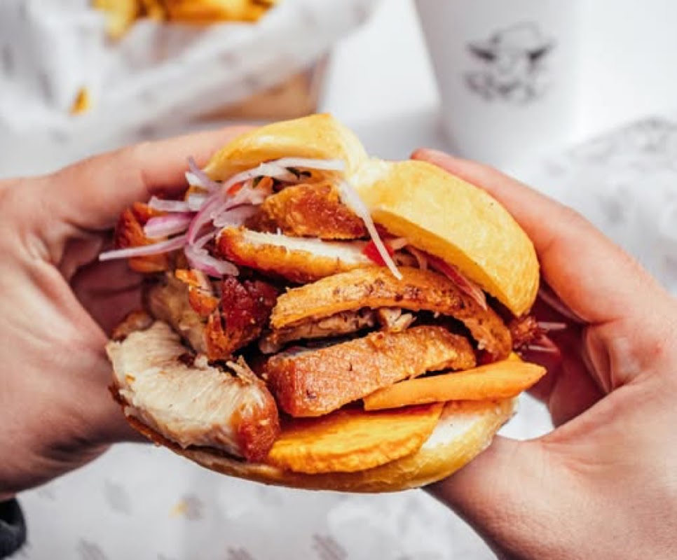Primer plano de la torta de chicharrón con salsa de chicha morada en La Lucha — detalle del relleno y el pan crujiente