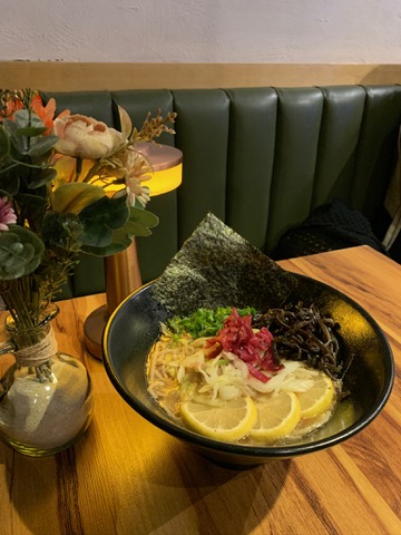 Primer plano del tazón de ramen vegano con trozos de orange chicken en Vegan Ramen Mei Del Valle, mostrando el caldo humeante y los toppings verdes