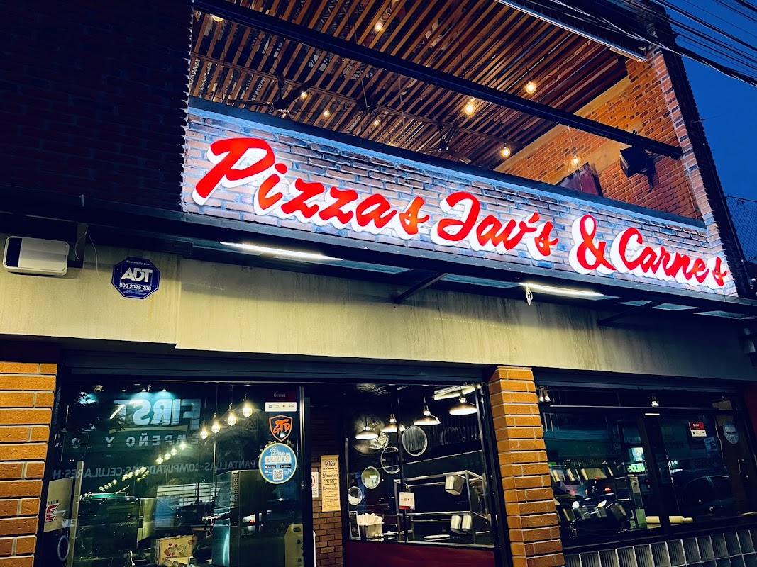 Pizzas Jav's - Sabor y Calidad, fachada iluminada y una pizza de arrachera en la mesa, mostrando la terraza al atardecer