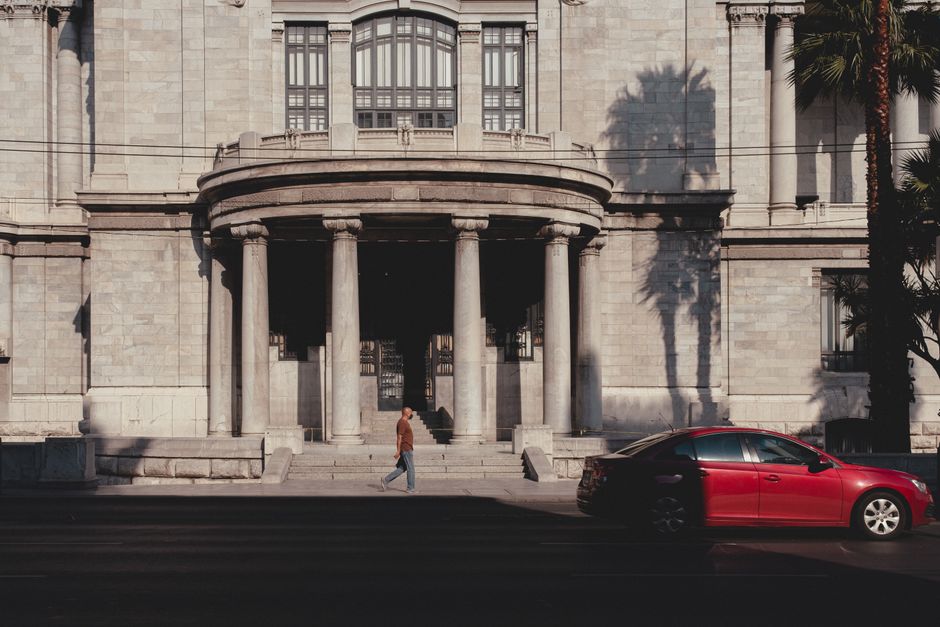Street view of historic building in Ciudad de México with a red car and pedestrian in the foreground.