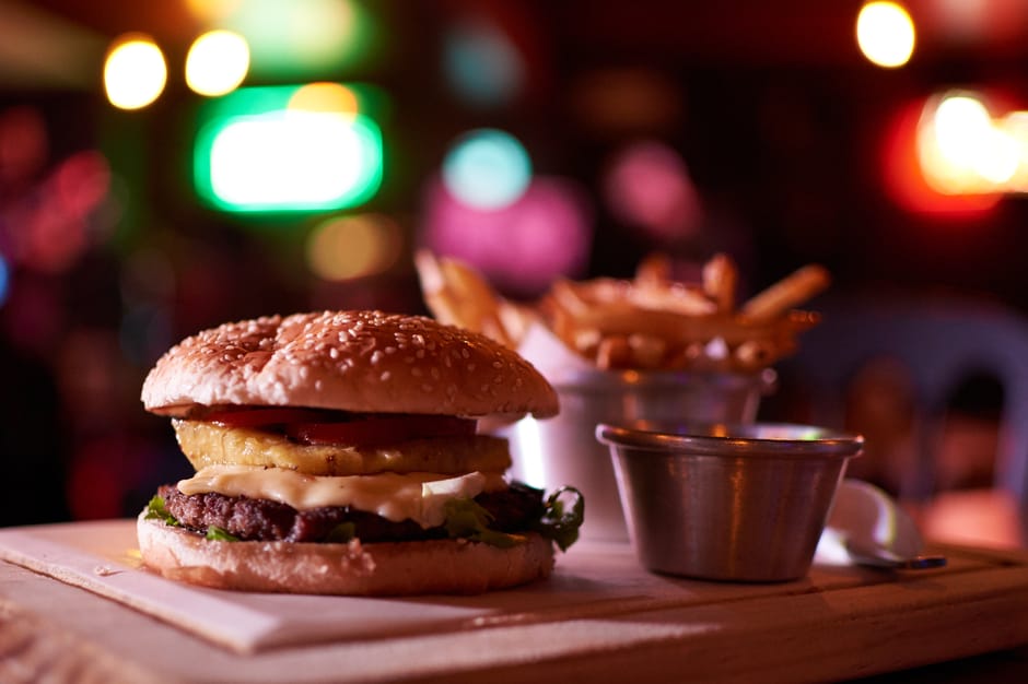 Delicious cheeseburger with pineapple and fries in a vibrant bokeh-lit restaurant setting.